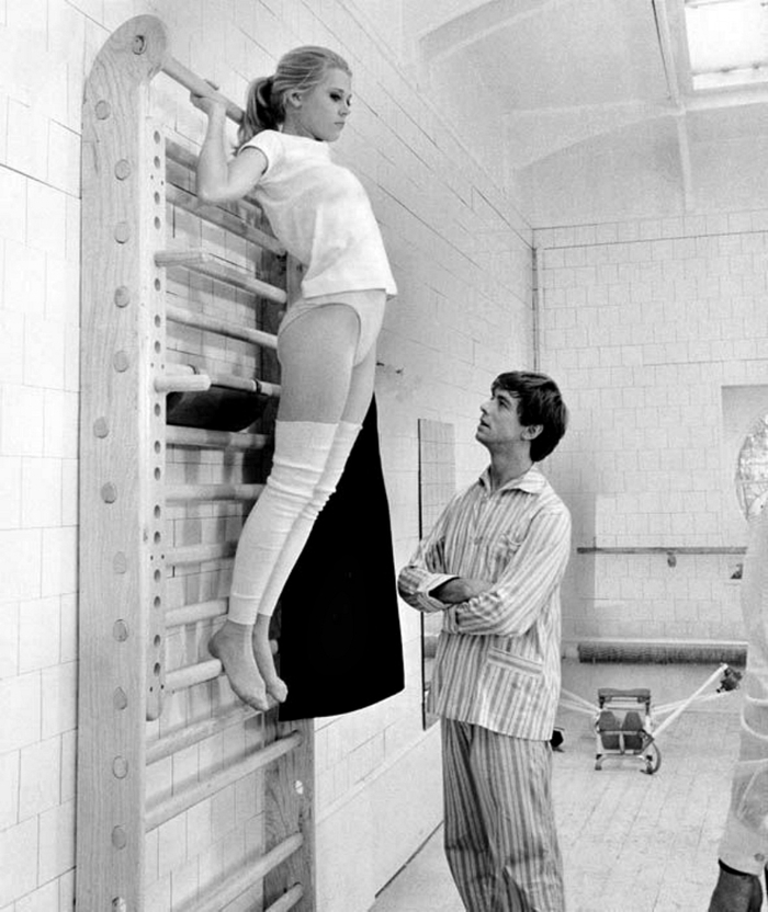 Джейн Фонда занимается гимнастикой. Рядом с ней стоит актёр Питер МакЭнери. 1960-е годы